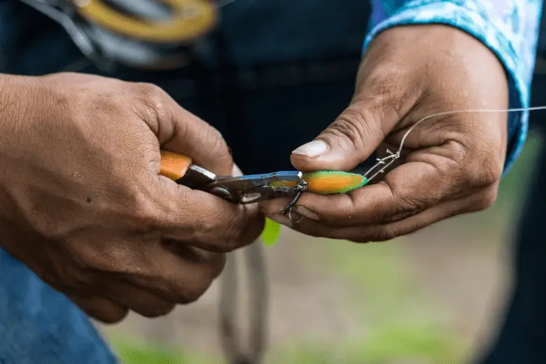 Angler tying a fishing hook to rubber worm lure using fishing pliers