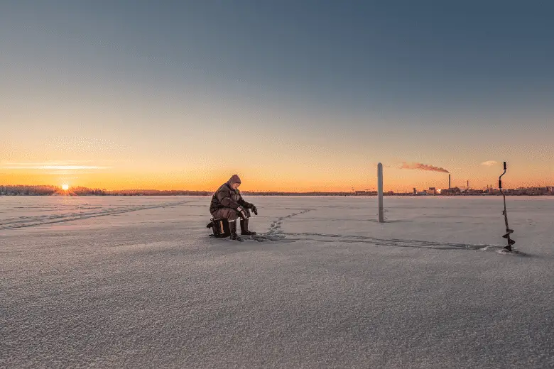 person sitting on stool on ice field near manual auger