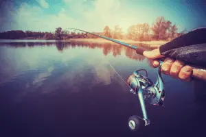 Hand on spinning reel overlooking a lake