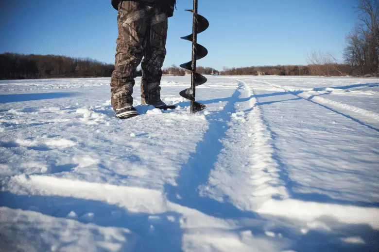 Ice fisherman drills hole with auger
