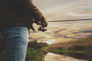 A man holding a spinning reel with water in the background