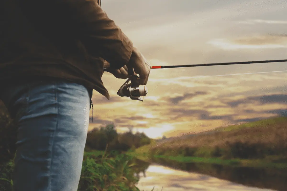 A man holding a spinning reel with water in the background