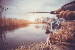 Hand with spinning and reel on the evening summer lake