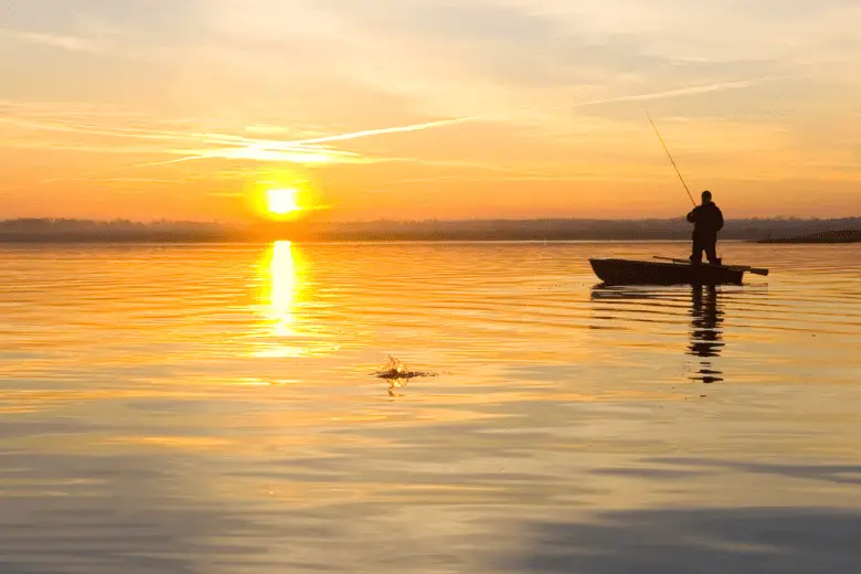 Man fishing on a boat with sunset in background