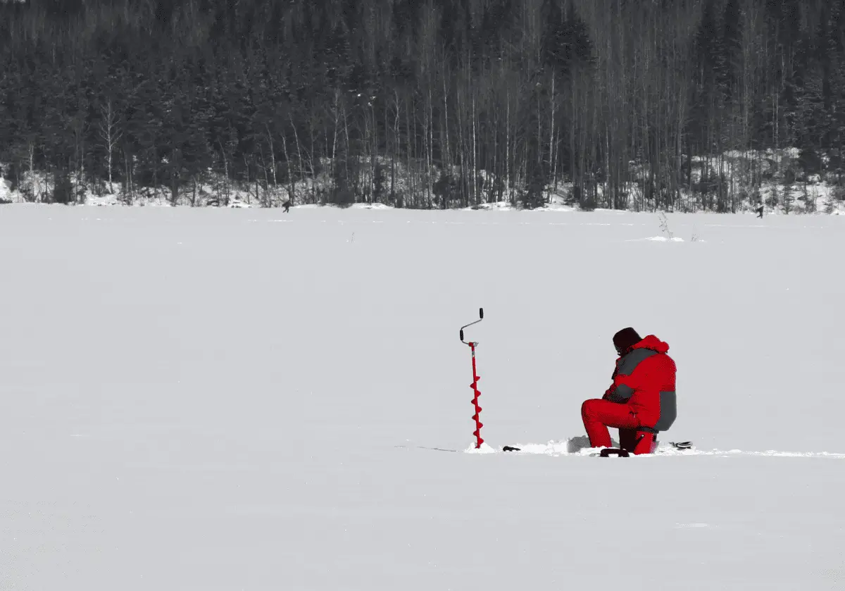 Man in red jacket ice fishing on a frozen lake
