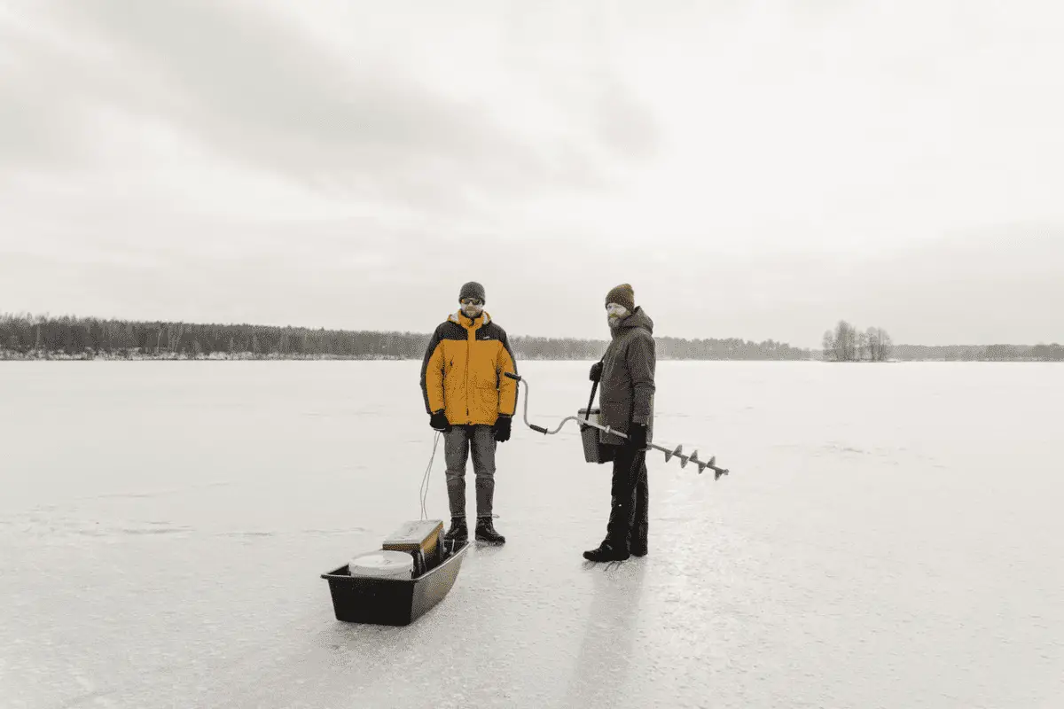 two men preparing to drill hole in frozen lake for ice fishing