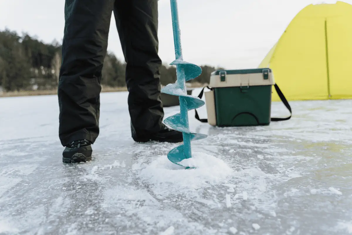 drilling a fishing hole in frozen lake for