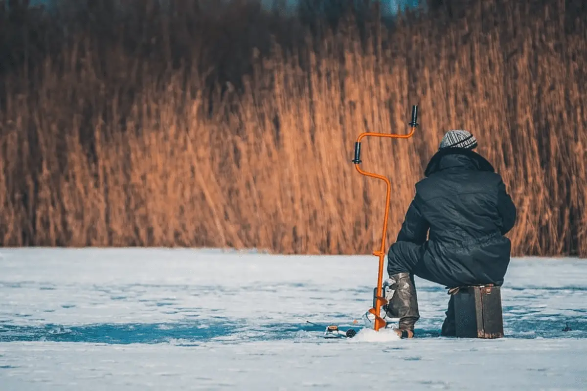 man using an auger to make an ice fishing hole