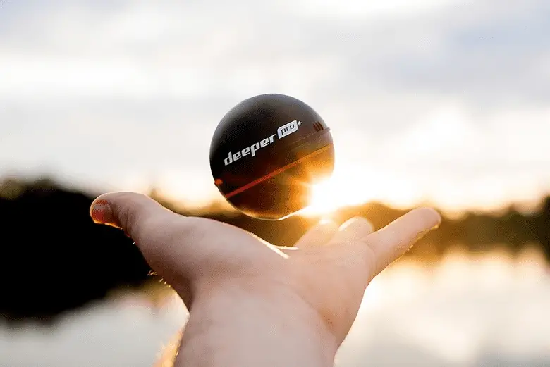 man holding a fish finder in front of a lake sunset