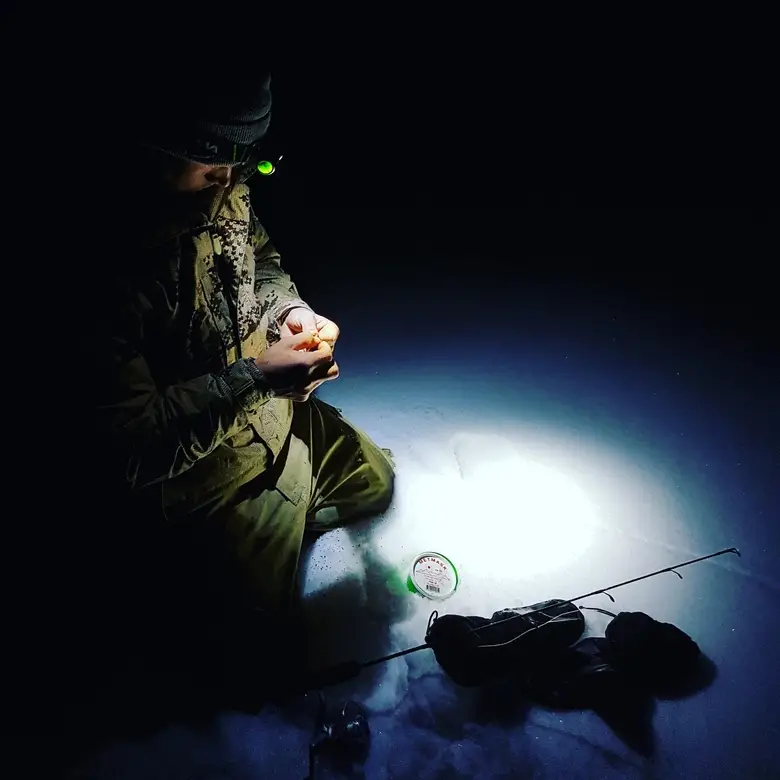 man preparing for ice fishing at night with a flashlight