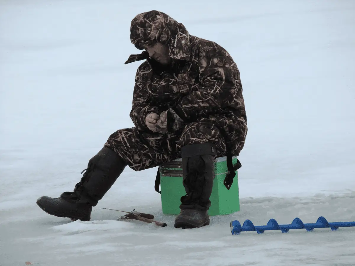 man putting on ice fishing gloves in the middle of a frozen lake