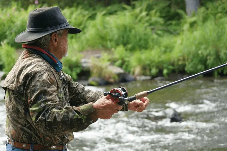 senior fisherman in camo clothing fishing near the river