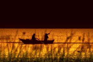 two men fishing from a small boat at sunset