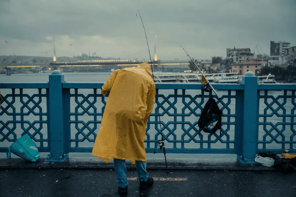 angler in yellow rainjacket fishing from the bridge