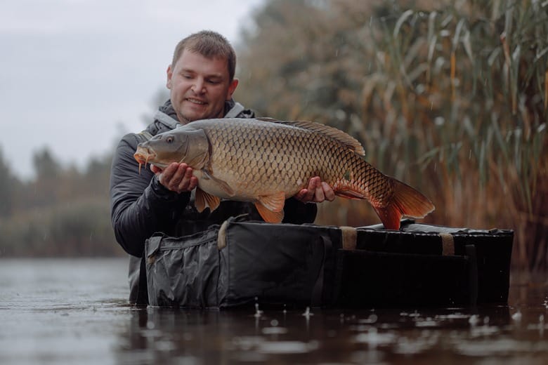 man holding a fish in the river while it's raining