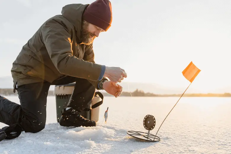 A man kneeling on the ice with a fishing pole.