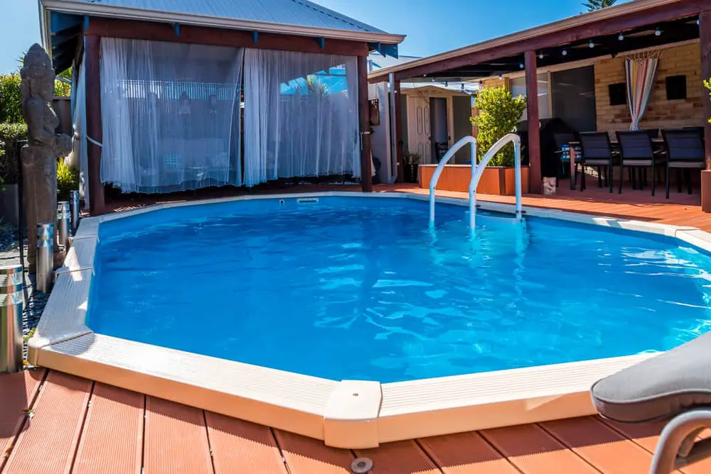 A swimming pool in a backyard with a wooden deck.